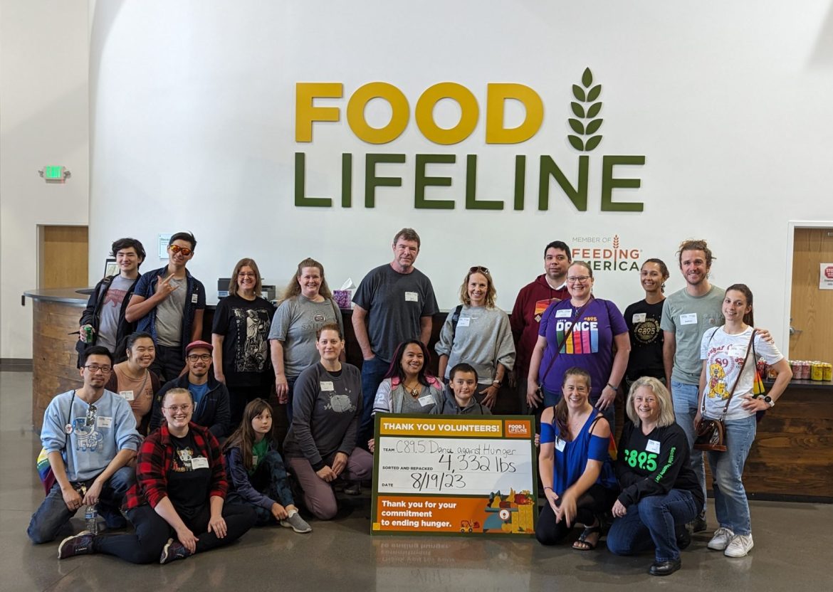 A large group of volunteers standing in front of a sign that says "Food Lifeline" with a smaller sign saying how many tons of food they packed.